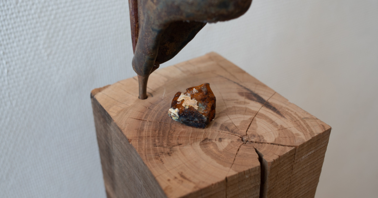 Een metalen beeldhouwwerk bovenop een houten blok met een mineraal