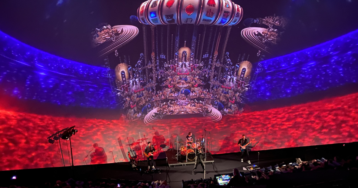 Een liveband speelt op een podium met kleurrijke projecties op de achtergrond.