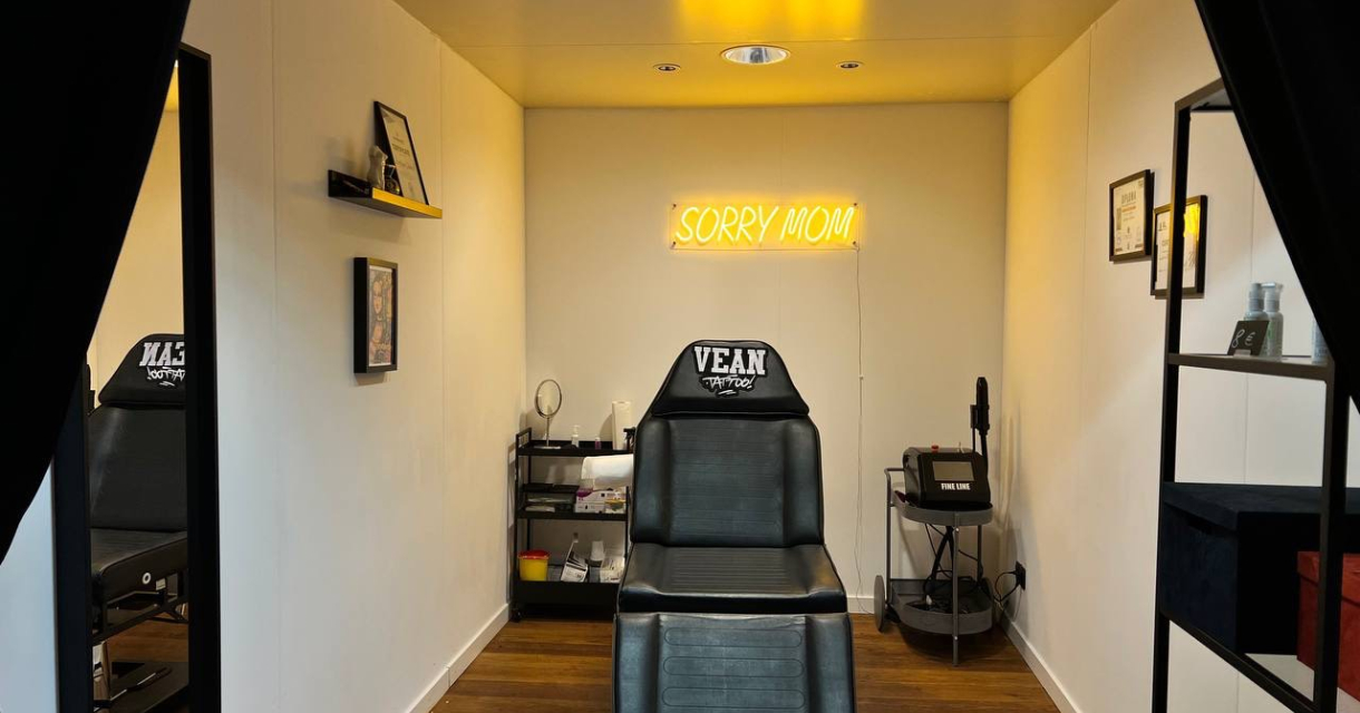 A corner view of a tattoo studio featuring a neon sign 'Sorry Mom'.