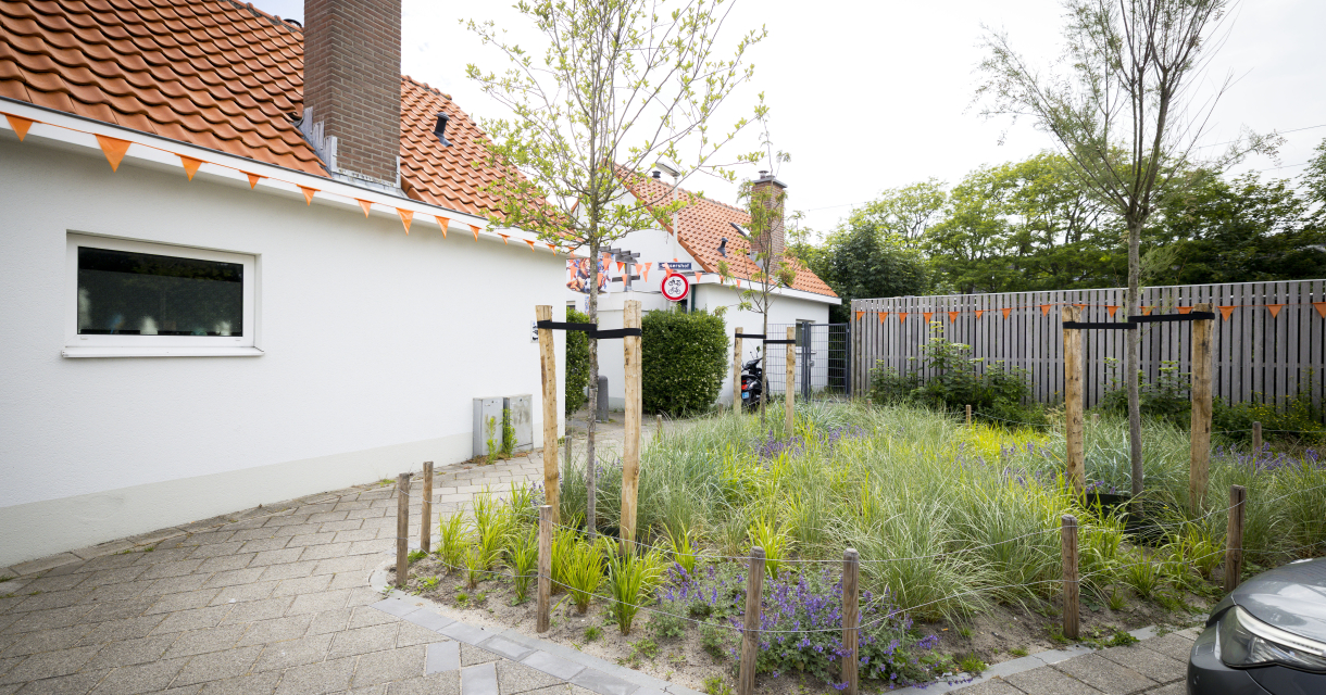 Een huis op Scheveningen met een rood dak en een groene tuin met bloemen.