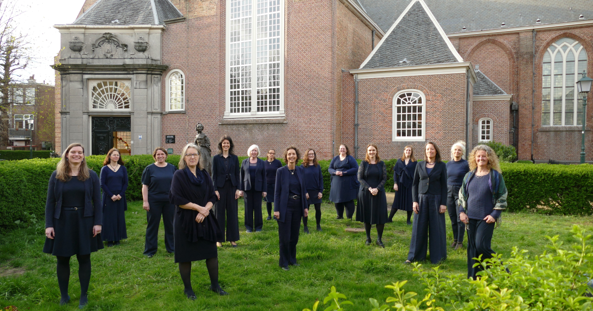 Vijftien vrouwen in donkere kleding staan in een tuin achter een gebouw.