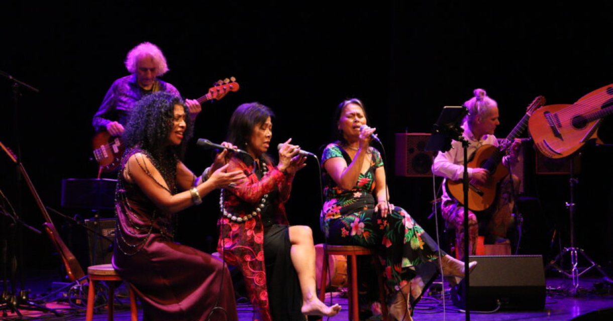 Vrouwen zingen op een podium met muzikanten erachter
