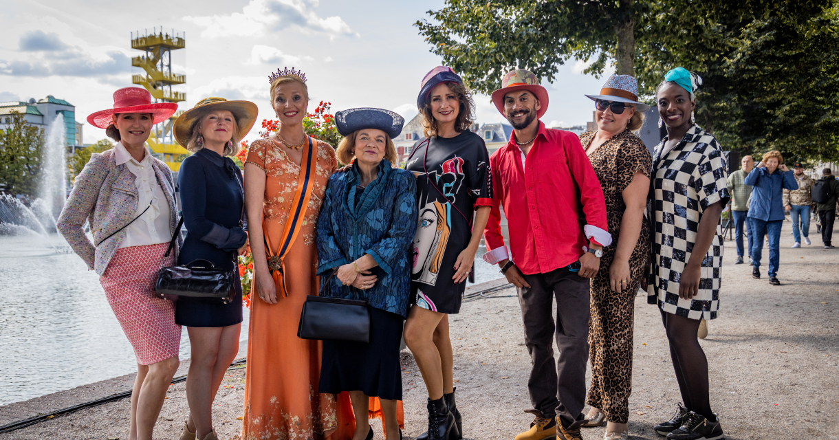 Een diverse groep mensen poseert in kleurrijke hoeden bij een fontein.
