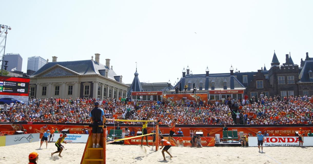 Spelers in oranje shirts tijdens beachvolleybalwedstrijd.
