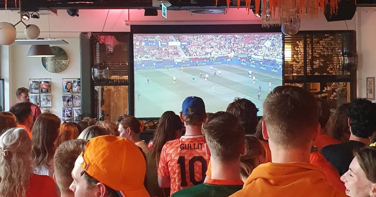 Groep mensen in oranje kijken naar een voetbalwedstrijd.