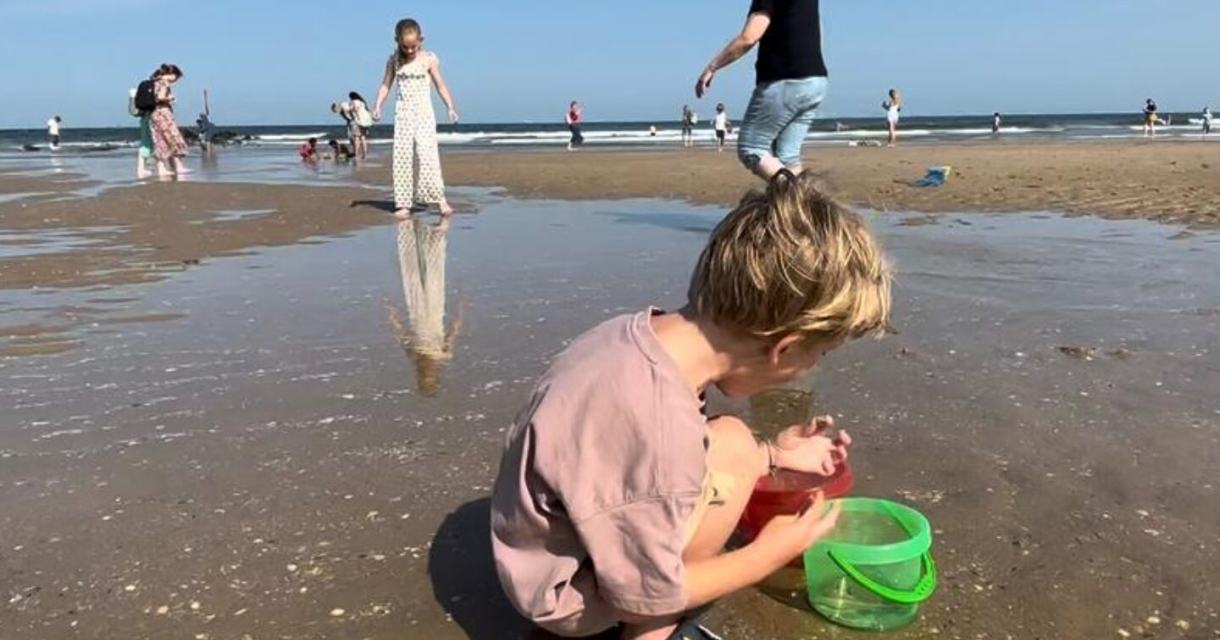 Een kind speelt met een emmer op het strand bij Scheveningen.
