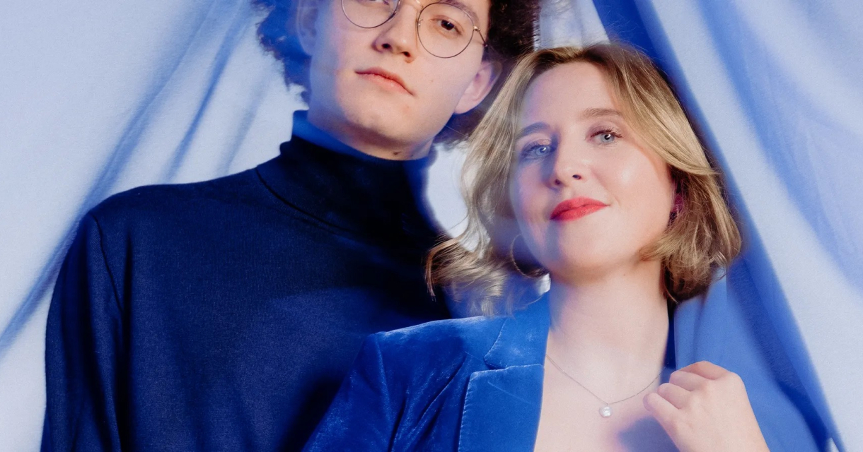 A woman in a blue blazer and a man in a blue shirt are standing together.