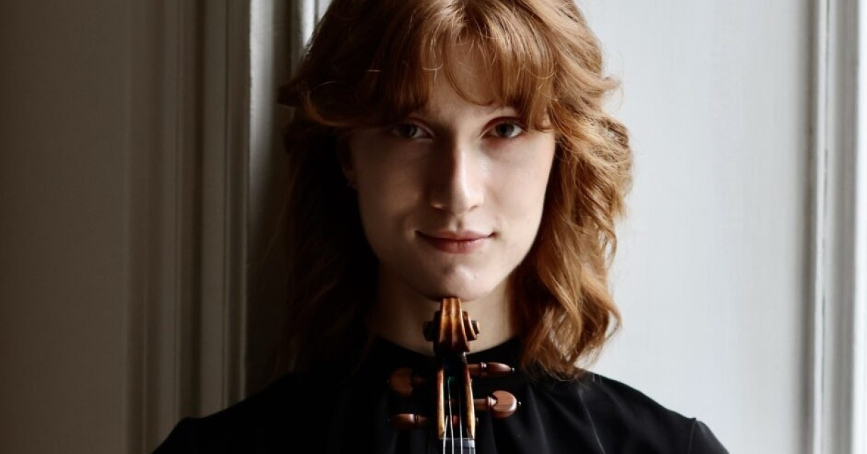 Een jongere vrouw met rood haar houdt een viool vast
