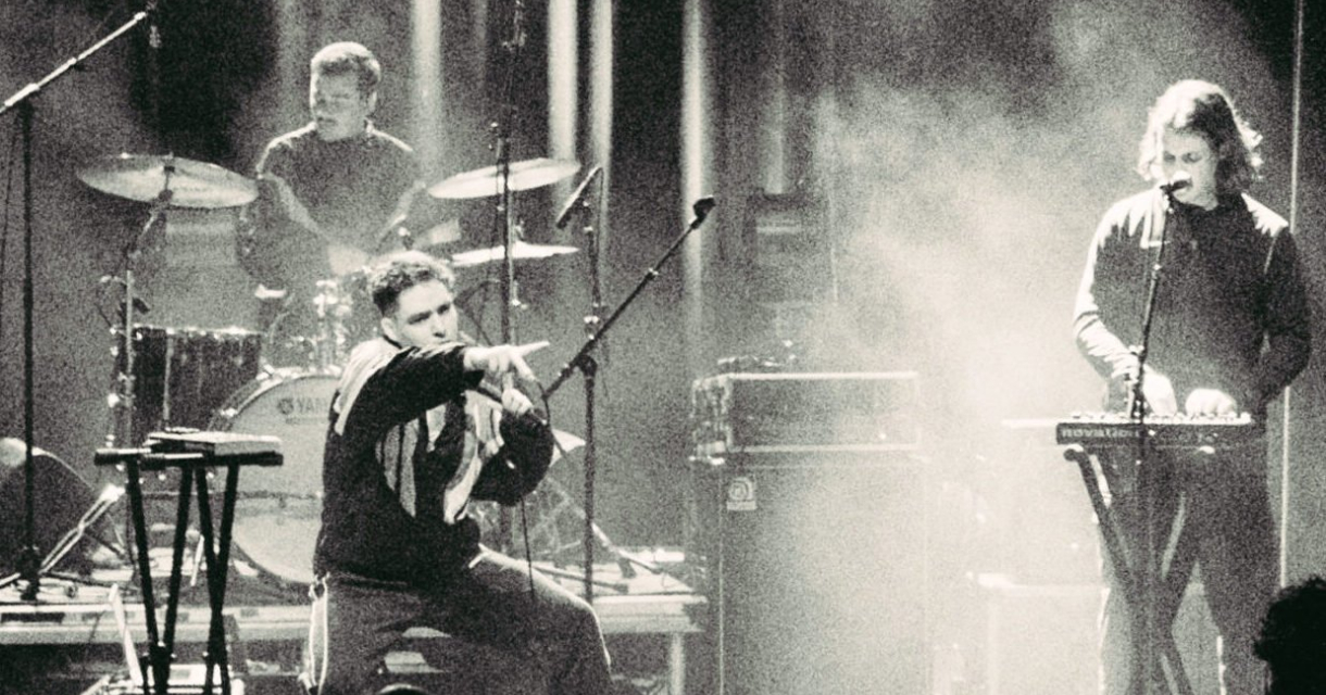 Drie muzikanten spelen op een podium voor een publiek.