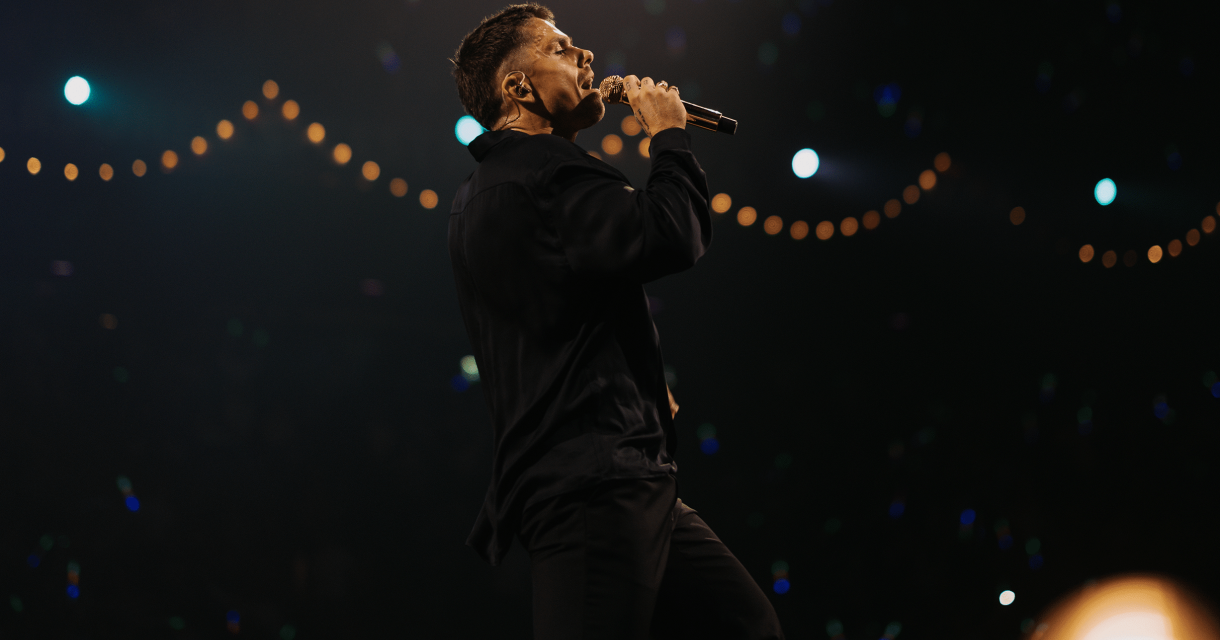 Een zanger staat in de spotlight en zingt met een microfoon.