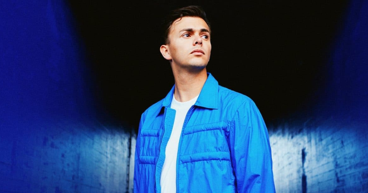 Jongeman staat in een blauwe gang met een neutrale uitdrukking.