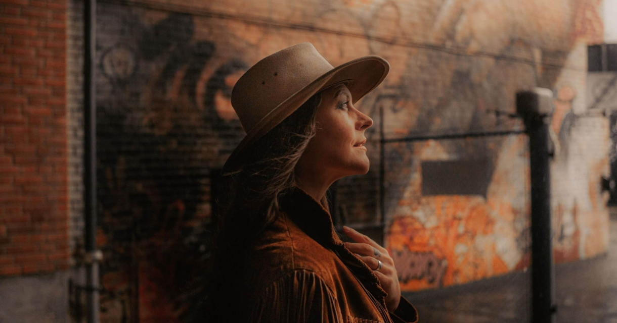 Vrouw met hoed staand voor een kleurrijke graffiti muur