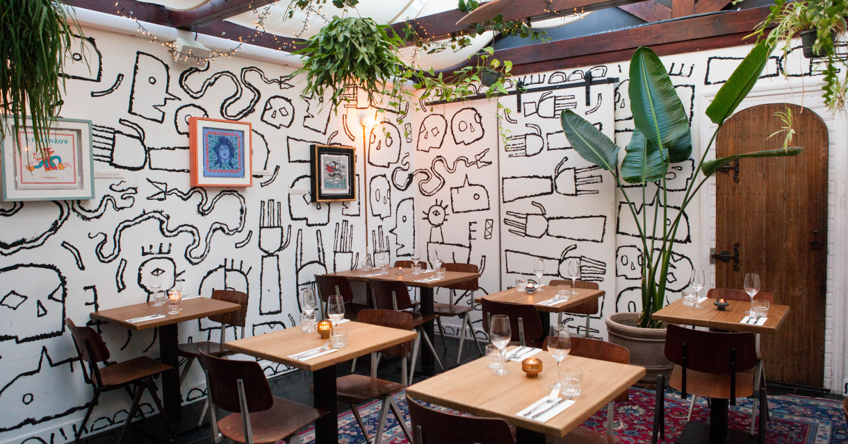 Cozy restaurant featuring artistic wall painting by Jamal Armand and plants.