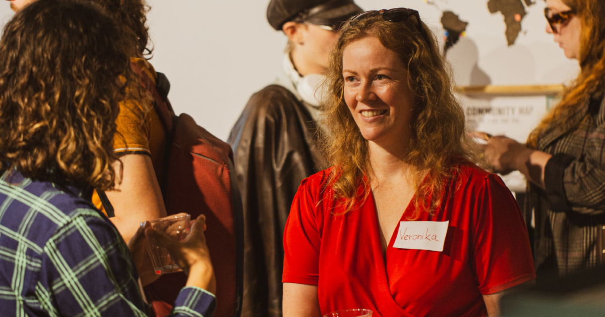 Een vrouw met krullend haar in een rode jurk glimlacht op een evenement.