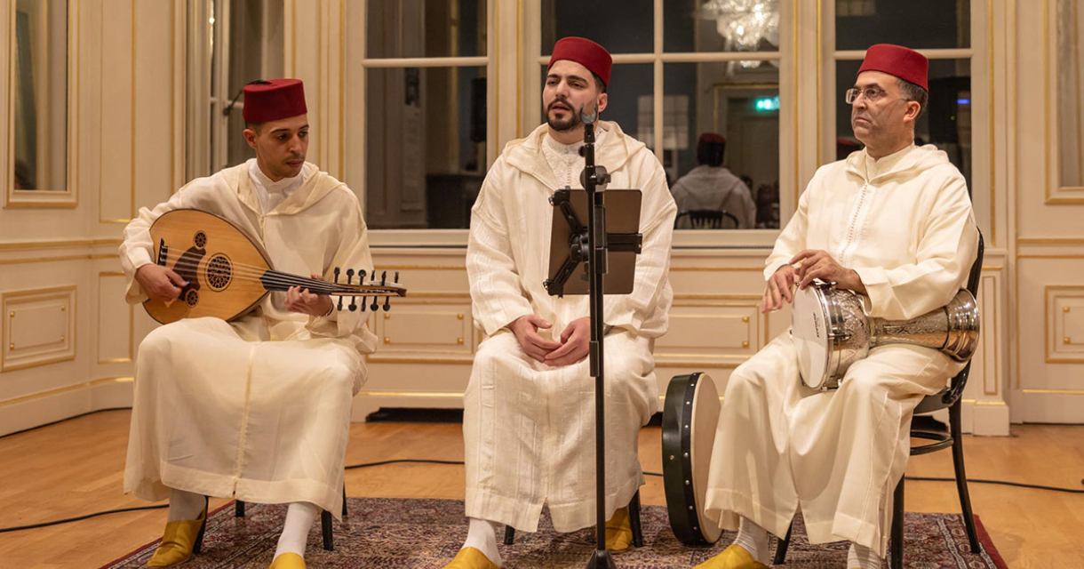 Drie muzikanten in traditionele kleding spelen instrumenten in een zaal.