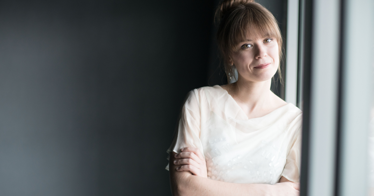 Vrouw met een lichte blouse leunt tegen het raam.