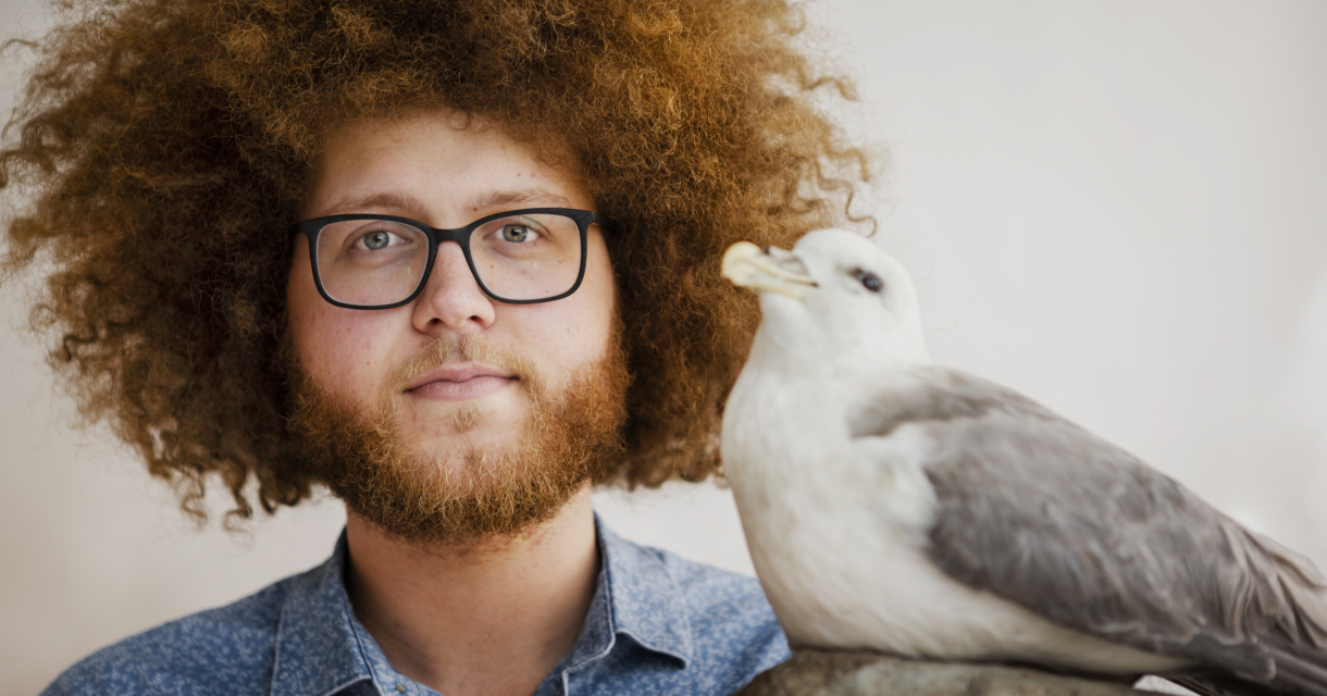 Man met krullend haar en een meeuw naast zich