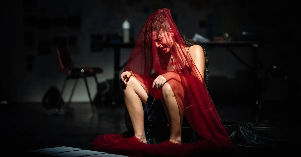 A woman sitting with a red veil, visibly sad.