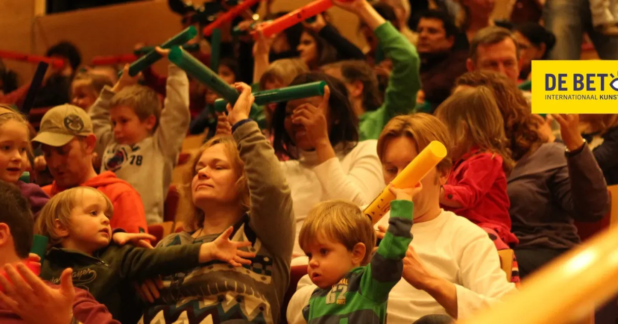 A group of children and adults in the audience with colorful musical instruments.