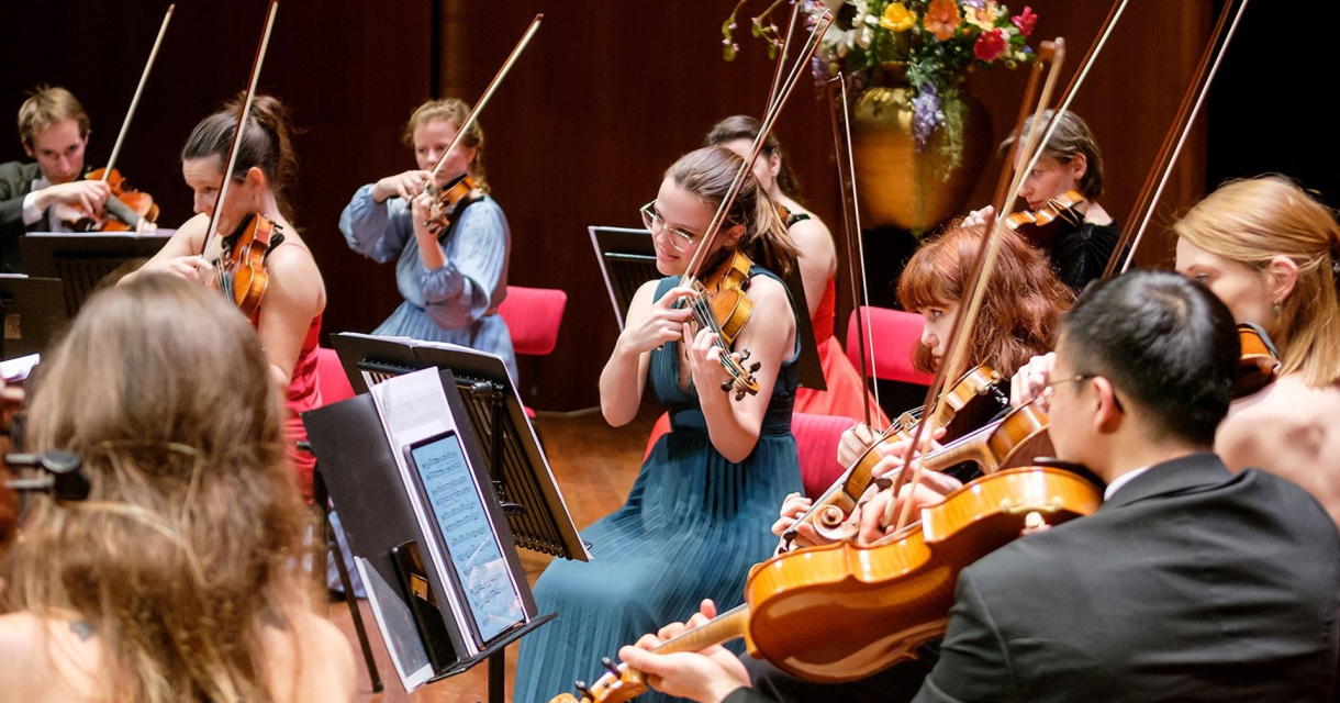 Strijkersensemble met vioolspelers in concertzaal, gekleed in galakleding en gefocust op hun muziekpartijen