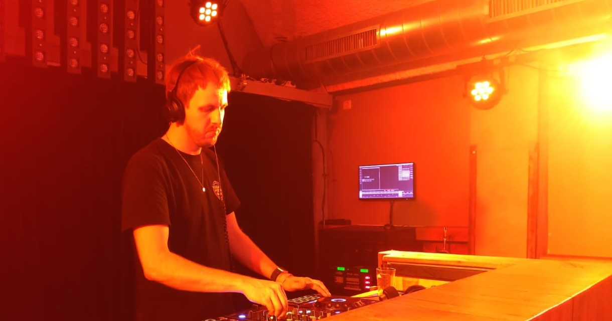 Een dj draait muziek op een mengpaneel in warme verlichting.