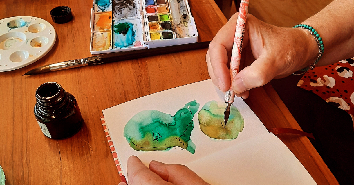 Een hand schildert groene aquarel vlekken in een notitieboek.