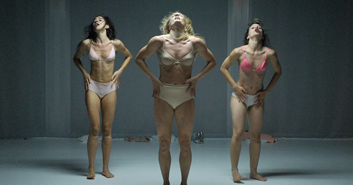 Drie vrouwen in lingerie dansen in een neutrale ruimte.