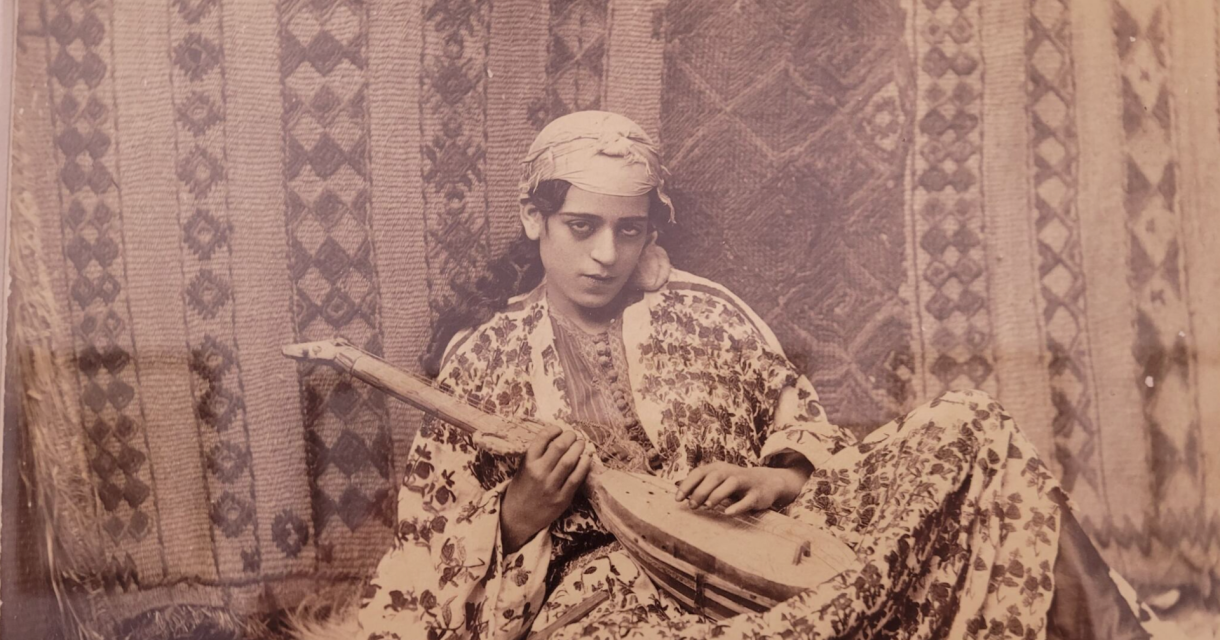 Een vrouw in traditionele kleding houdt een muziekinstrument vast.