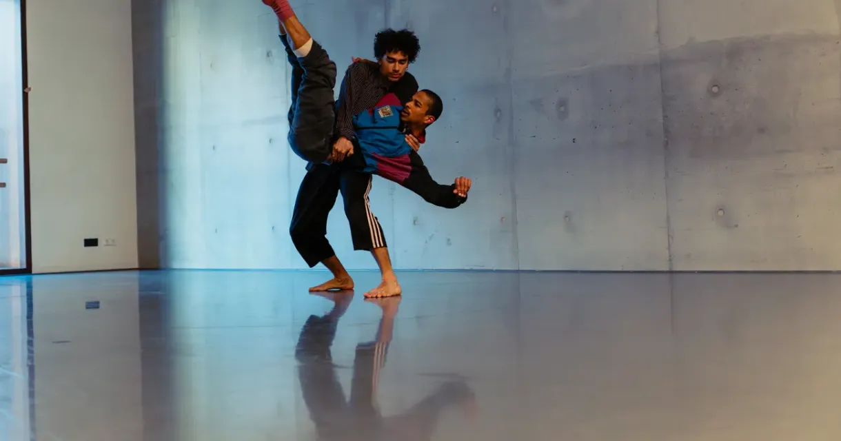 Twee dansers voeren een beweging uit in een dansstudio.