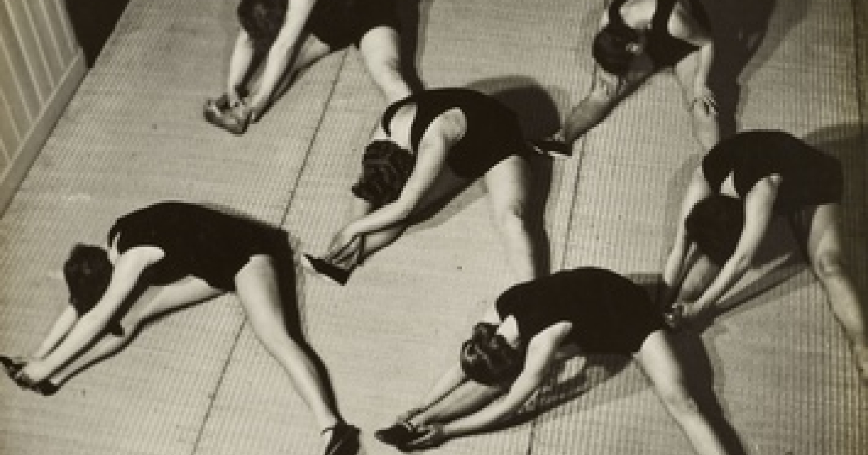 Zes dames in zwarte sportoutfits rekken hun benen.