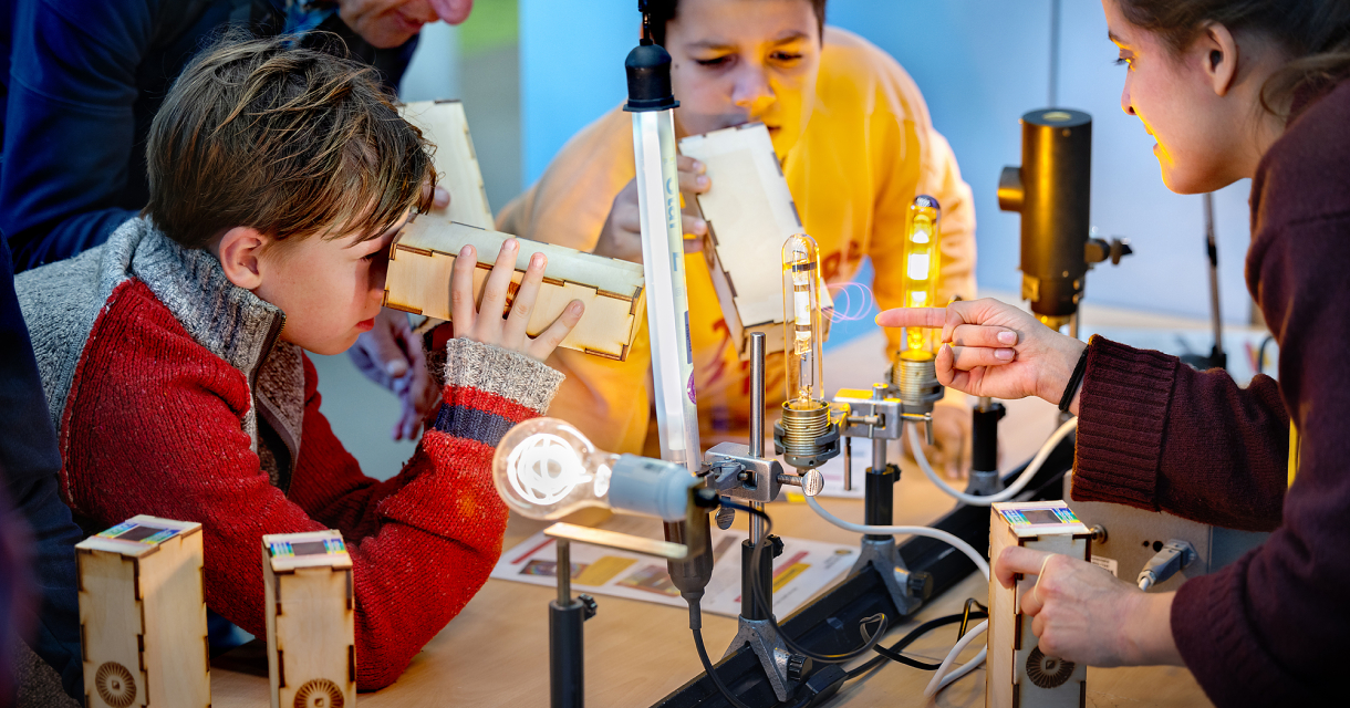 Kinderen en een oudere man bezig met technische proefjes.