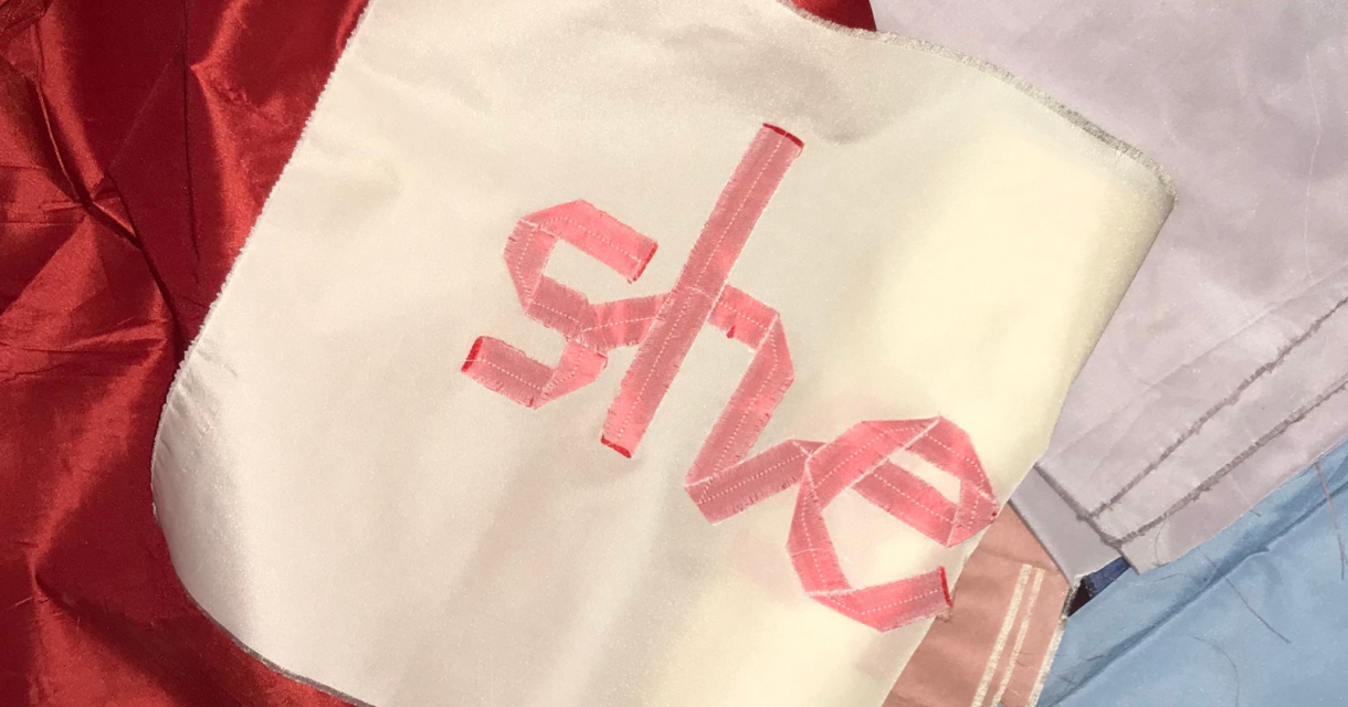 Een vlag met de woorden 'she' in roze op een witte achtergrond.
