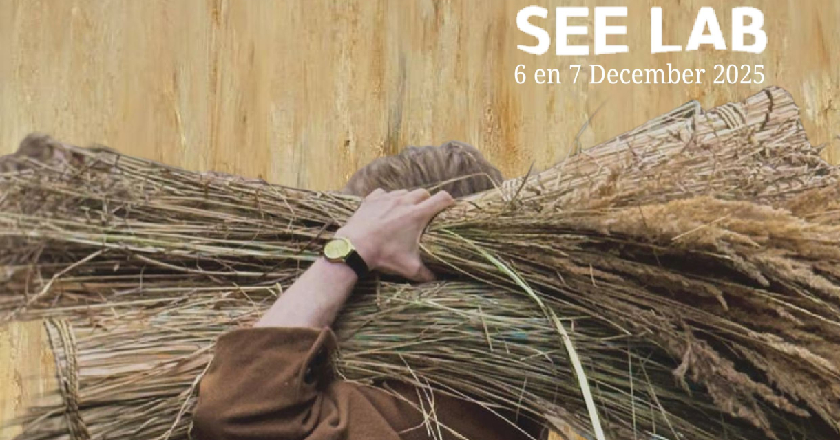 Foto van een man in een bruine pij in een korenveld met een bos graan op zijn schouder