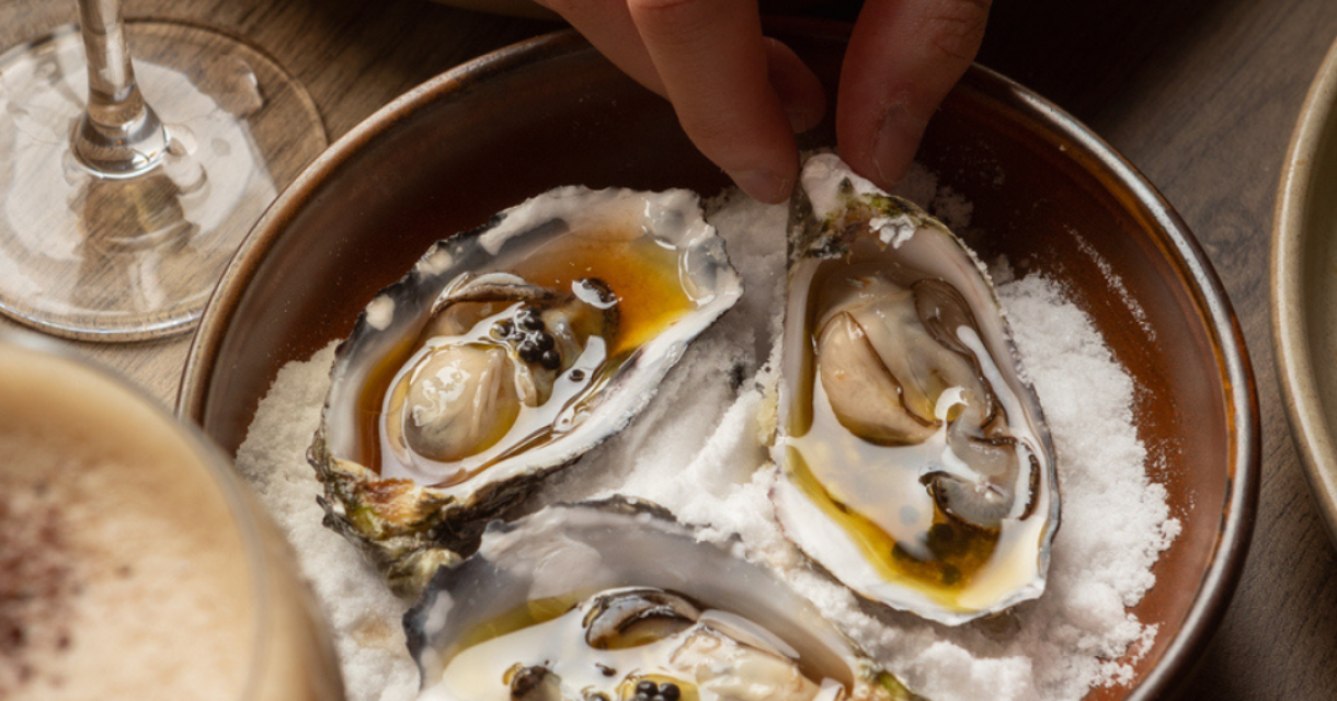 Hand van iemand die een oester uit een schaal pakt.