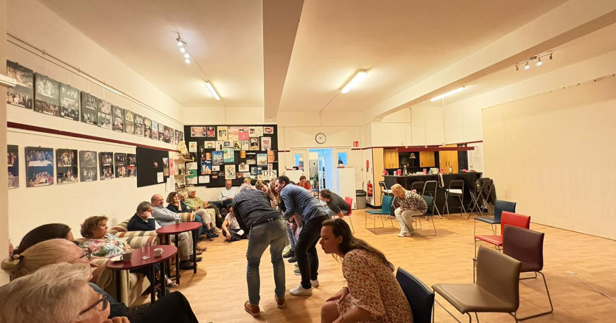 Groep mensen in een buurtcentrum met houten vloer, felle verlichting en kunst aan de muren