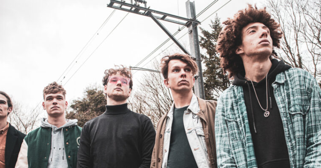 Vijf jonge mannen staan in een industriële omgeving.