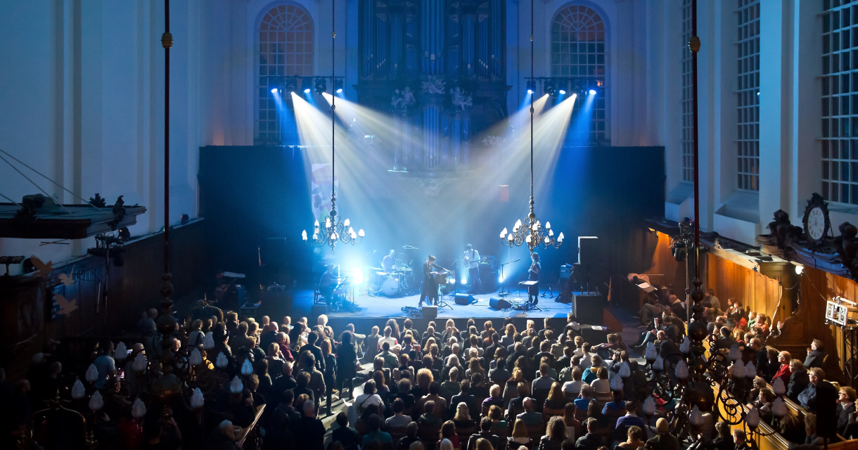 Crossing Border Festival in een grote zaal met publiek waar het podium blauw verlicht is.
