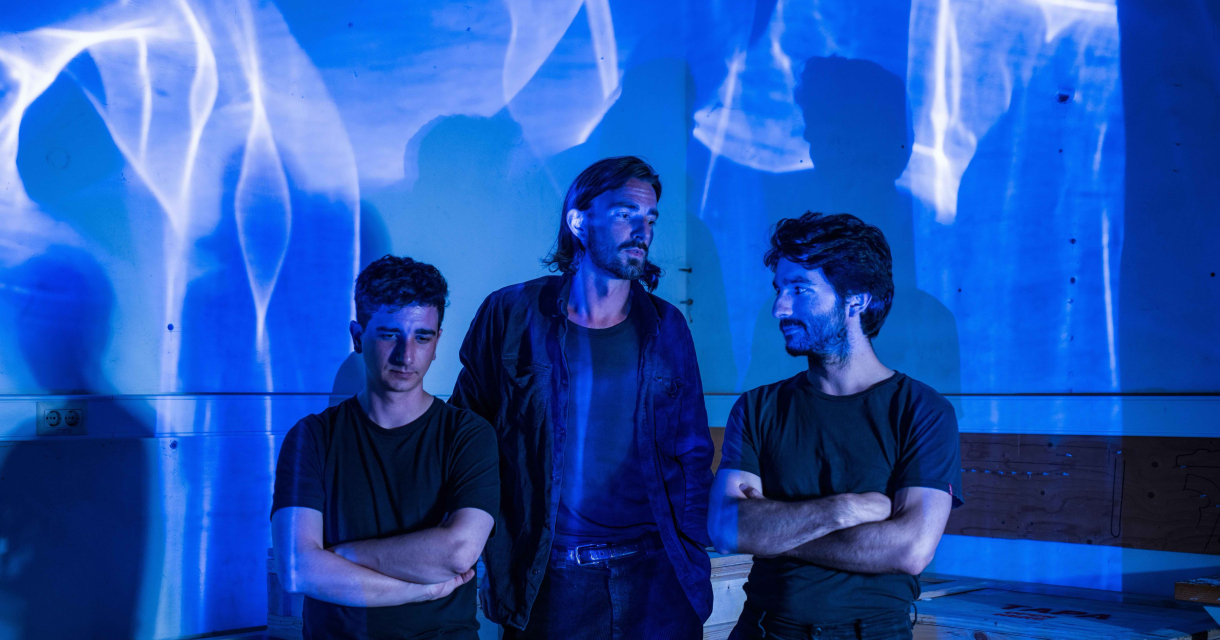 Drie mannen staan naast elkaar met blauwe lichtprojecties.