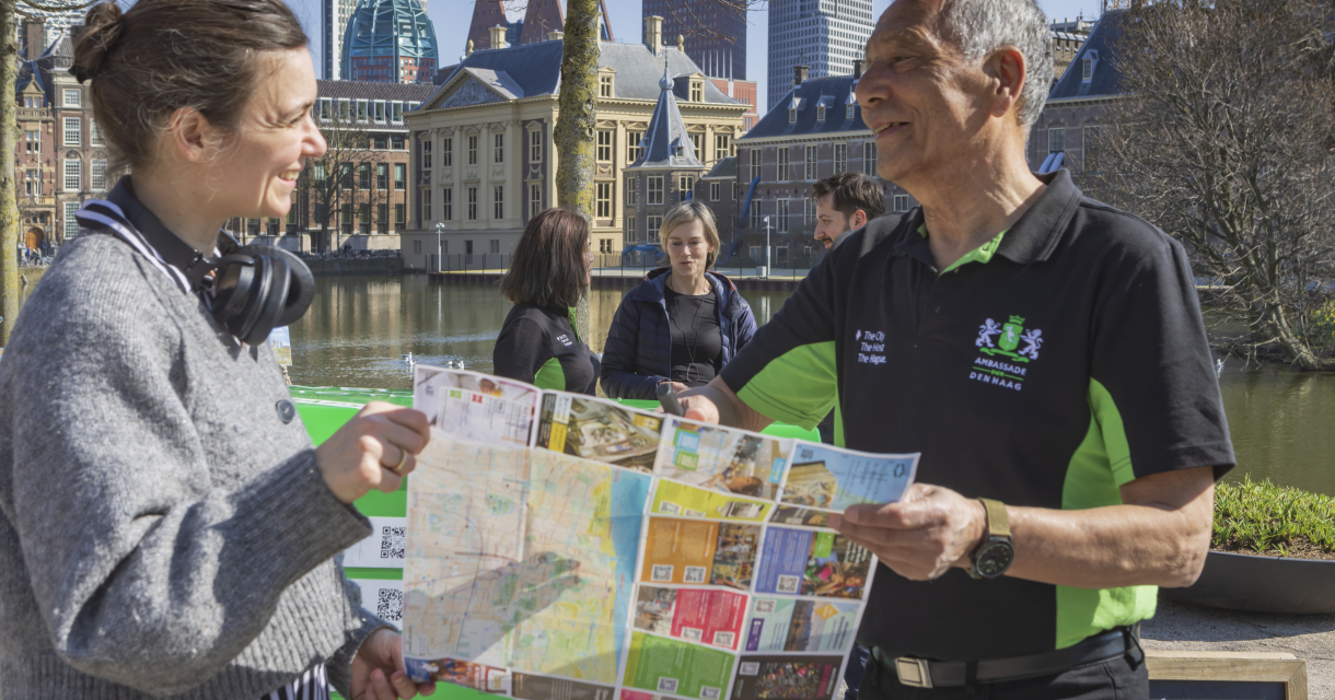 Een vrouw en een Haagse cityhost bekijken een plattegrond aan de Hofvijver.
