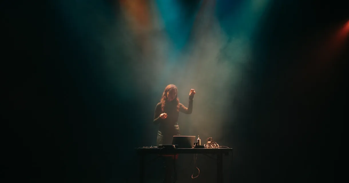Een vrouw met lange haren staat achter een tafel met DJ-apparatuur.