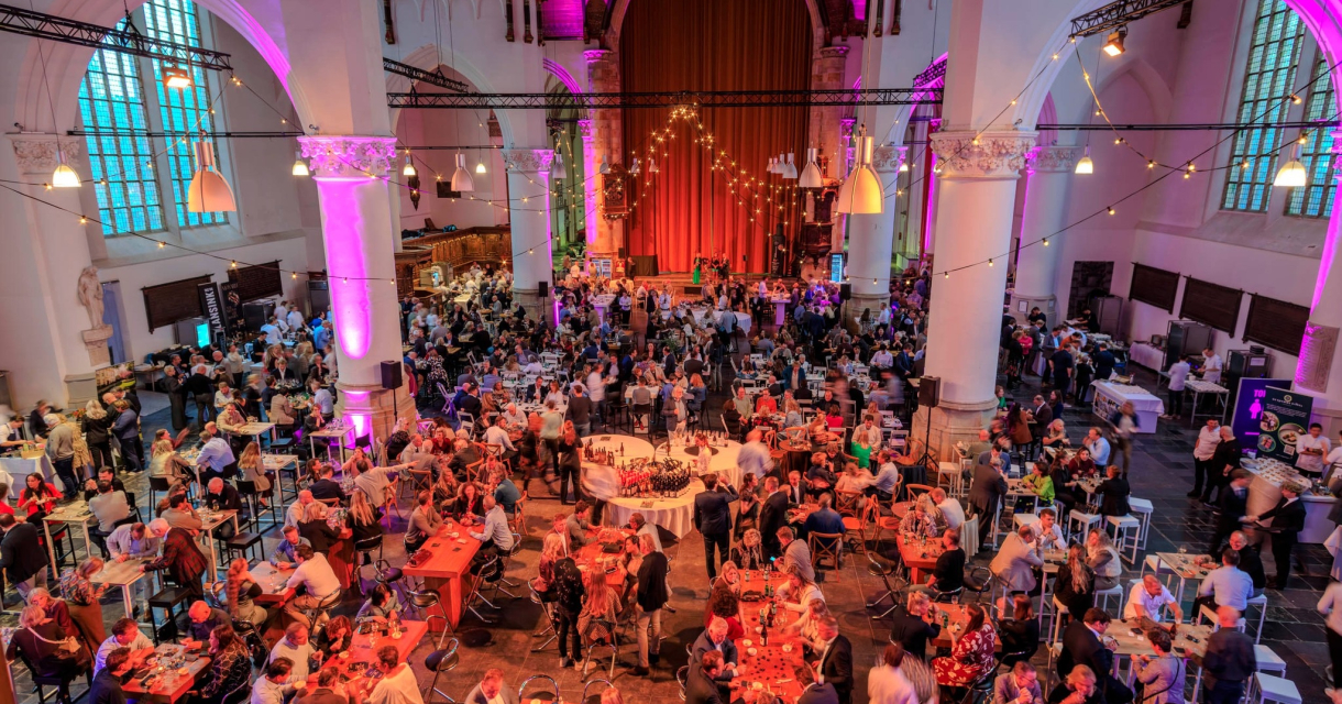 Grootste SterrenProeverij van Nederland in de Grote Kerk. Een druk bezochte feestlocatie met mensen en tafels.