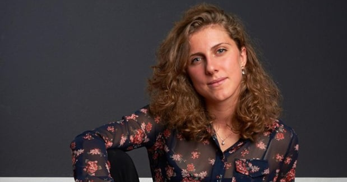 Een vrouw in een bloemenoverhemd zit met een gitaar.