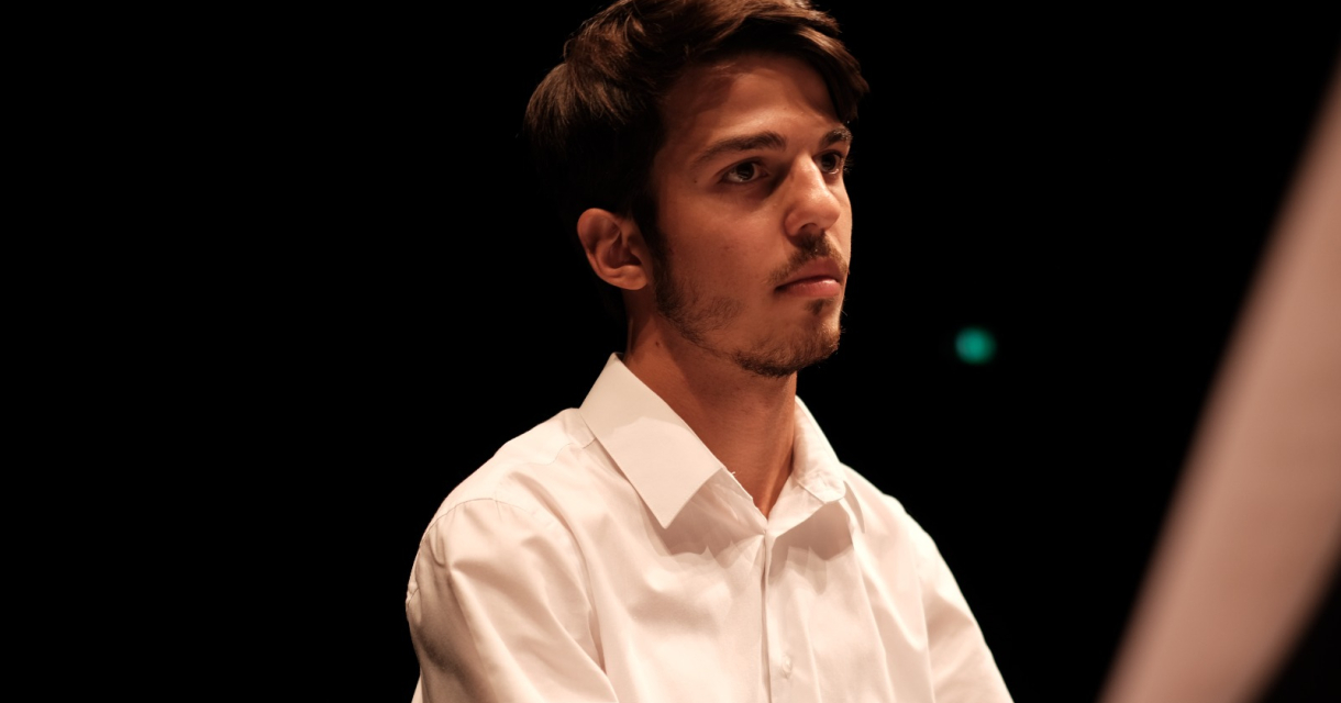 Een jonge man met een witte blouse kijkt serieus. 