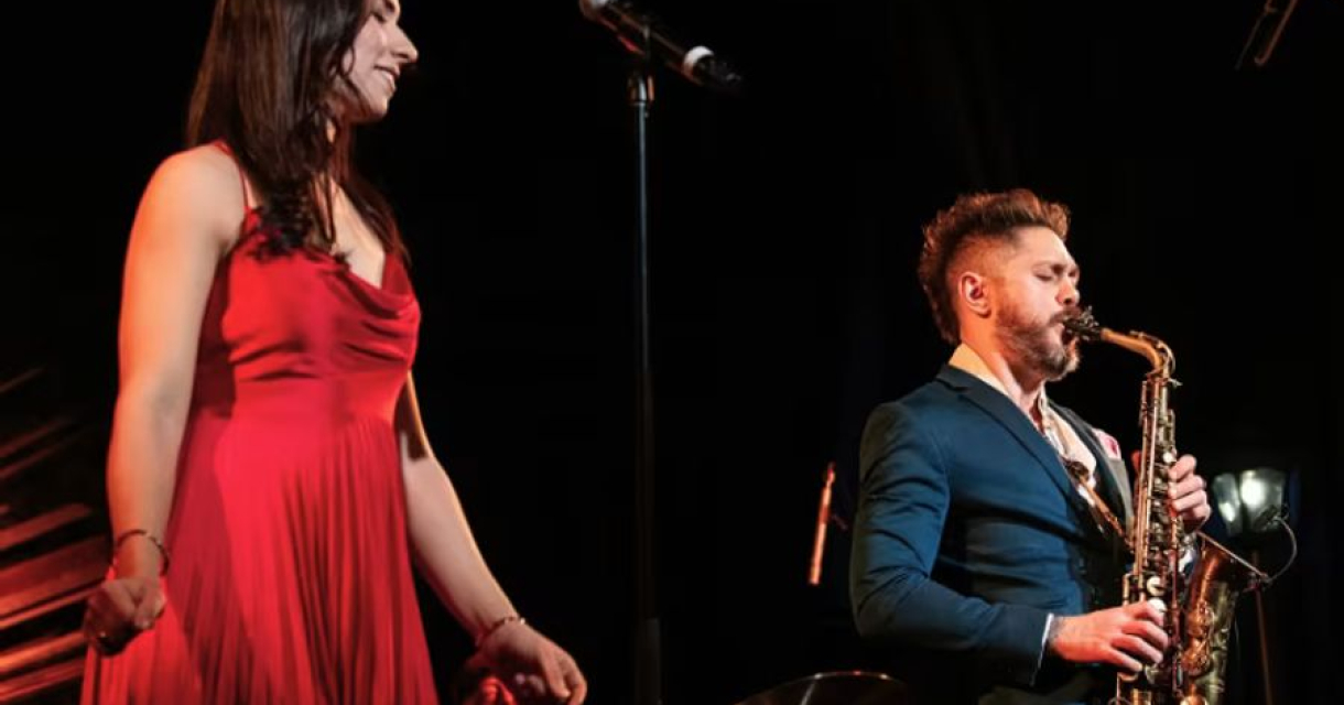 Een vrouw in een rode jurk zingt terwijl een man saxofon speelt.