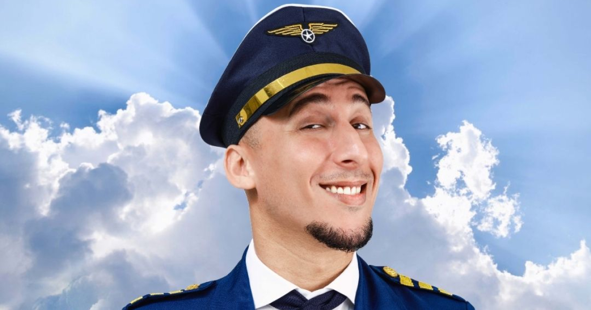 Een glimlachende man in een pilotenuniform met een hoed.