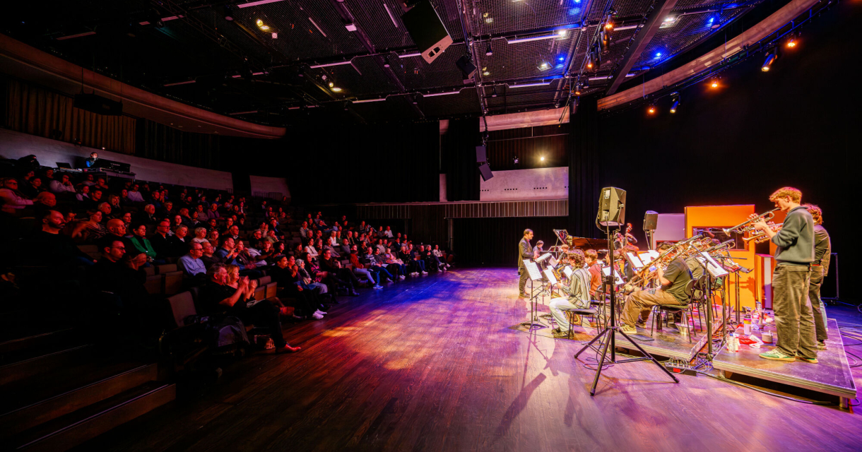 Een druk theater met een band die optreedt voor publiek.