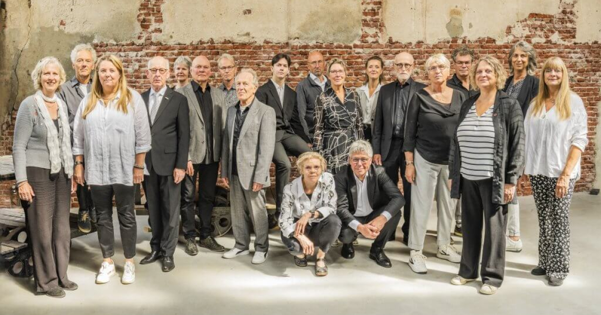 Een groep van twintig mensen posed voor een muur.