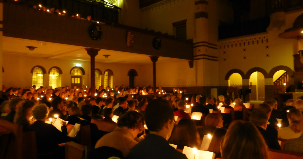 Kerkdienst bij kaarslicht met volle banken, mensen houden brandende kaarsen vast in sfeervol verlichte ruimte