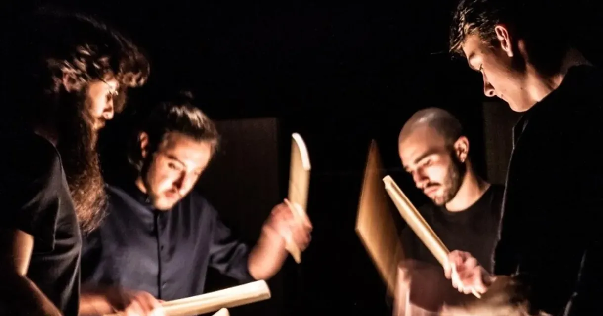 Vier muzikanten zijn bezig met het spelen van percussie in een donkere ruimte.