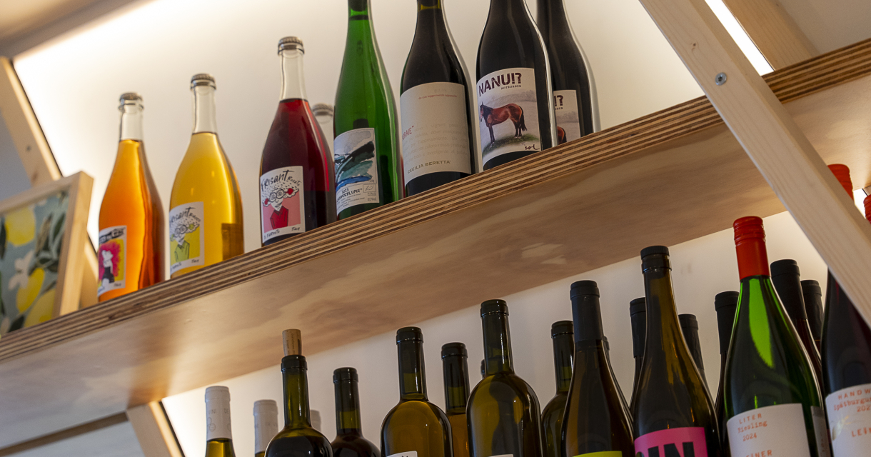 Een assortiment wijnflessen in diverse kleuren op een houten plank.